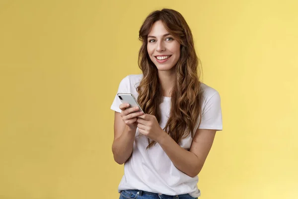 Entusiastiska snygg urban flicka bära vit t-shirt stående casual leende glad kamera SMS håll smartphone bläddra sociala medier foder stå gul bakgrund bläddra nätverk — Stockfoto