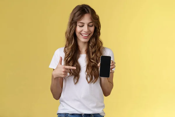 Förbryllad karismatisk glad ung kvinnlig bloggare visa vad foto app använda redigera sociala medier profil hålla smartphone tittar pekfinger mobiltelefon tom skärm leende roade — Stockfoto