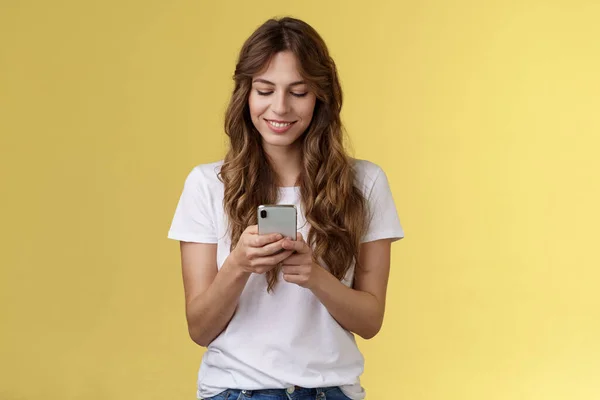 Härlig feminin anbud kaukasiska flicka vit t-shirt jeans hålla smartphone SMS:a meddelande flickvän ler glad utseende ömt härligt leende mobiltelefon skärm gul bakgrund — Stockfoto