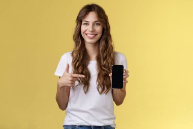 Kızın akıllı telefona ihtiyacı var. Neşeli, rahat, kaygısız kadın uzun kıvırcık saç stili cep telefonunu işaret eden cep telefonunu tut gülümseyerek uygulamanın sarı arka planda nasıl çalıştığını açıkla.