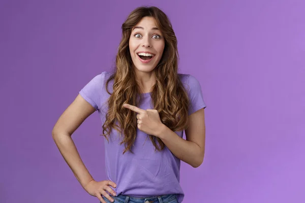 Lively excited enthuasitic good-looking woman curly hairstyle open mouth fascinated look admiration joy share awesome place location pointing left smiling broaldy thrilled purple background — Stock Photo, Image
