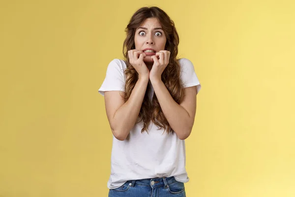 Asustado tímido inseguro inseguro europeo chica rizado corte de pelo agarre manos cara morder dedos mirar asustado sorprendido de pie estupor sin palabras temblando miedo aterrorizado amarillo fondo — Foto de Stock