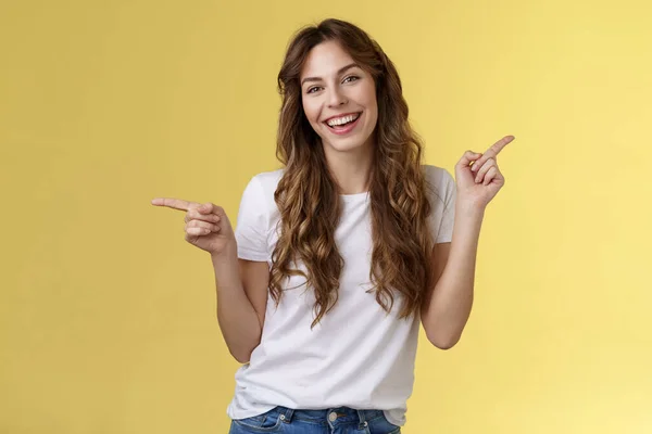 La chica tiene dos sugerencias apuntando hacia los lados. Alegre carismático de pelo rizado atractiva mujer señalando los dedos índice izquierdo derecho introducir productos promocionales sonriendo ampliamente animado recomendar anuncio — Foto de Stock