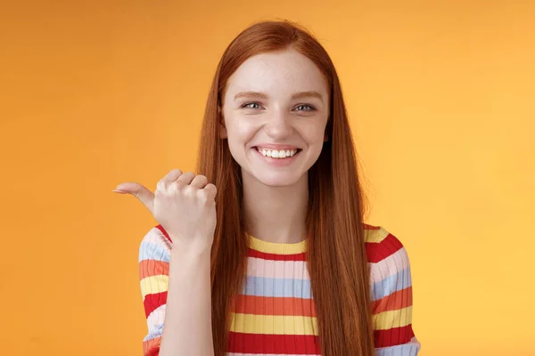 Chica señalando a la izquierda persona fresca puede ayudar a sonreír encantado mirada amigable cámara discutir interesante proyecto introducir amigo durante la conversación de pie feliz sonriendo fondo naranja —  Fotos de Stock