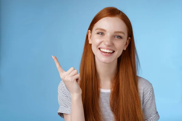 Boldog karizmatikus vörös hajú nevető fiatal lány szórakozás keres gondtalan beszélgetés megvitatása új termék eladó mutató mutatóujját mutatja másolás tér reklám, álló kék háttér — Stock Fotó