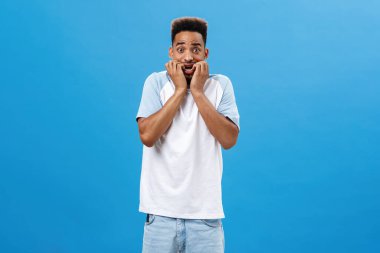 Korkmuş, koyu tenli, fobisi olan, tırnaklarını yiyen, gözleri büyüten, korku ve korkudan titreyen, sıradan bir yaz tişörtü giymiş, korku içinde duran adamın portresi.