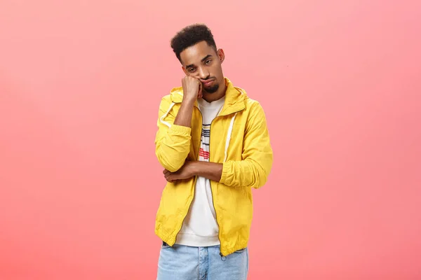 Estúdio tiro de entediado indiferente boa aparência jovem escuro pele cara com barba e afro penteado inclinando a cabeça no punho olhando com tédio descuidado para baixo choramingando sentindo apatia sobre a parede rosa — Fotografia de Stock