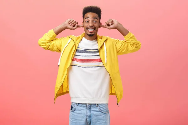 Close ears it be loud. Portrait of happy excited handsome stylish african bearded guy in trendy yellow jacket closing hearing with index fingers and smiling broadly awaiting bang over pink background — 图库照片