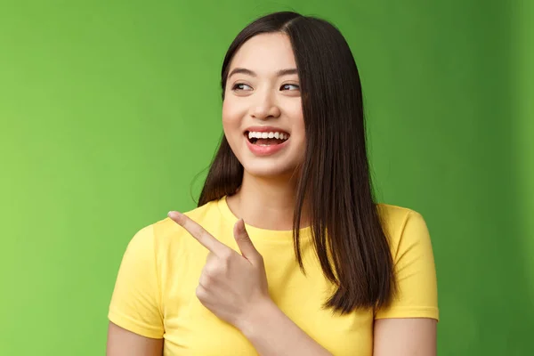 Primer plano alegre amigable asiático extrovertido chica divirtiéndose, apuntando a su vez a la izquierda divertido, animado hablando, discutir amigos interesante evento, de pie verde fondo charlando despreocupado entretenido — Foto de Stock