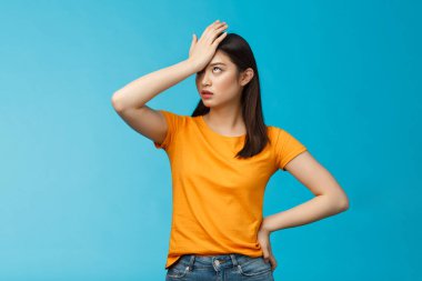 Annoyed arrogant asian girl punch forehead make facepalm sign, roll eyelids irritated pissed, cannot stand lame talks look disappointed ingorant, unwilling to listen, stand blue background