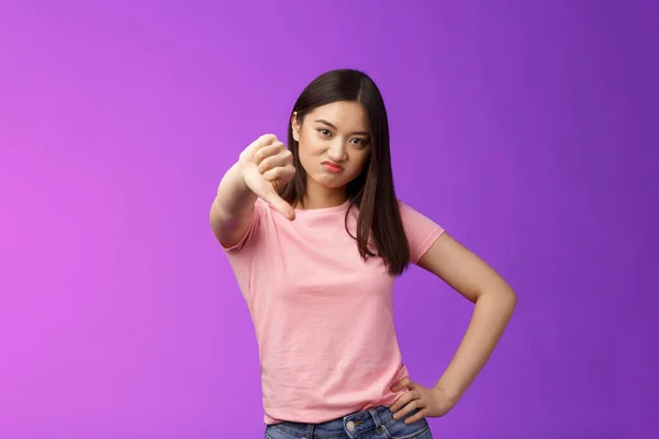 Coxo, muito mau. Desagradado julgamento asiático menina mostrar polegar para baixo, sorrindo, cringing de decepção, insatisfeito terrível desinteressante desempenho, queixar-se, stand roxo fundo — Fotografia de Stock