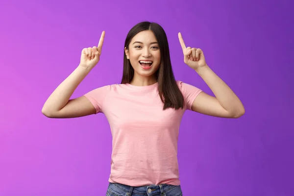 카리스마적 이고 잘생긴 미소짓는 아시아 소녀는 제품을 소개하고 손가락을 위로 향하고 광고를 보여 주며 웃으며 흥분되고 좋은 소식을 전하고, 연결을 공유하고, 보라색 배경을 알려준다 — 스톡 사진