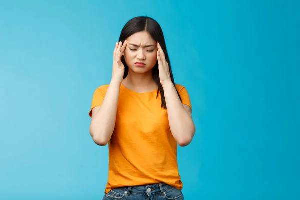 Vermoeide Aziatische vrouw donker kapsel cringe touch tempels, lijden enorme migraine nodig pijnstillers, pijnlijke hoofdpijn, duizelig voelen, staan blauwe achtergrond intens gedraineerd — Stockfoto