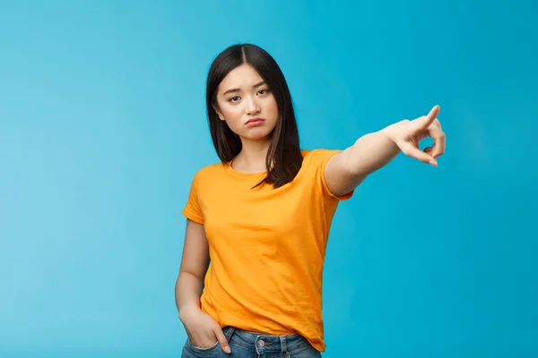 Tűnj el innen! Komoly kinézetű arrogáns elégedetlen parancsolgató ázsiai lány bemutató út-out, mutató oldalra mutatva mutatva mutatóujj megjelenés kamera kereslet szabadság, állni kék háttér tudatlan — Stock Fotó
