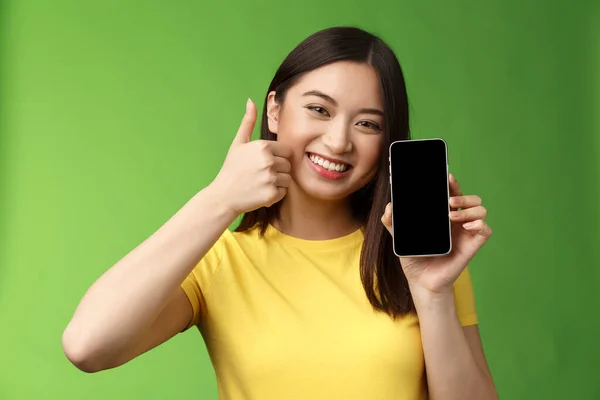 Närbild nöjd söt asiatisk flicka ger positiv feedback, tummen upp visar smartphone-skärmen, införa awesome ny app, rekommendera bra program, skryta slå poäng i spelet — Stockfoto