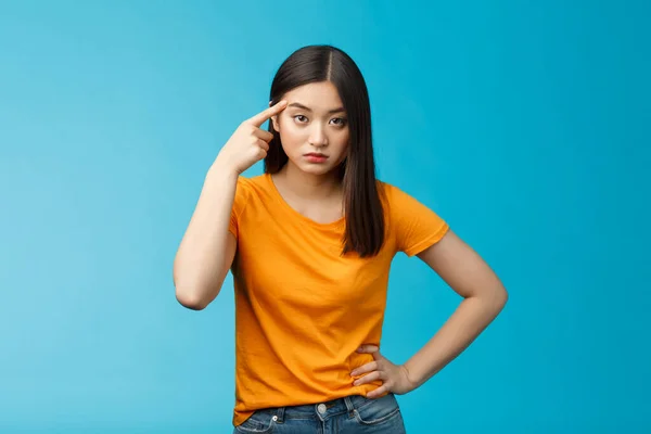 Pissed irritated asian girl look annoyed bend camera roll finger on temple stare camera bothered dismay, asking are you out mind, show person crazy weird, stand blue background — Stock Fotó