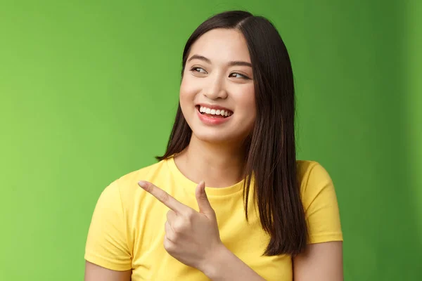 Amistoso saliente linda chica asiática teniendo divertida conversación, alegremente girar apuntando a la izquierda, indicar impresionante objeto fresco, discutir evento interesante, charlando sin preocupaciones, de pie fondo verde — Foto de Stock