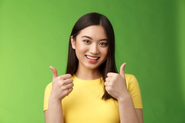 Destekleyici tatlı Asyalı kız arkadaş sevgilisini destekliyor. Sevgi gösterisi onay işareti, sevinçle gülümsüyor, iyi bir seçim gibi, mükemmel çabayı kabul et, arkadaşını cesaretlendir, yeşil arka planda dur.