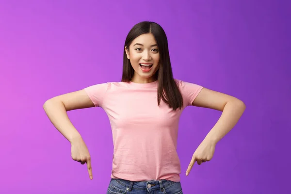 Animado entusiasta asiático morena mujer excitado diciendo acerca de impresionante promo, apuntando hacia abajo sorprendido, sonriendo alegremente recomiendan buen anuncio, indicando parte inferior anuncio —  Fotos de Stock
