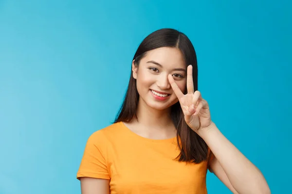 Positif petite amie asiatique mignonne et idiote posant photographie belle sourire, montrer signe de victoire de paix près du visage sourire amical, humeur enthousiaste insouciante, debout fond bleu en t-shirt jaune — Photo