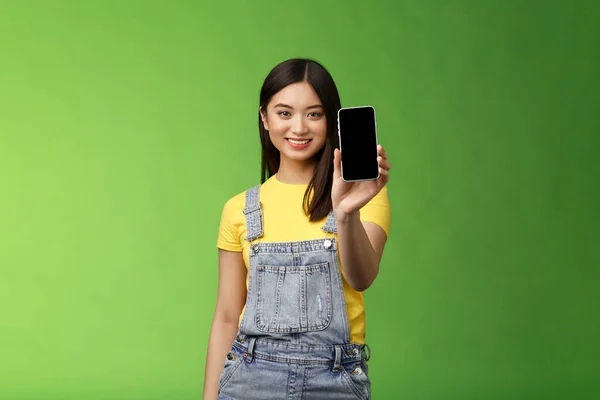 Självsäker övertygande snygg kvinnliga asiatiska införa smartphone app, förlänga handtag telefonarm, ler glad, rekommendera social profil, skryta egen blogg, grön bakgrund — Stockfoto