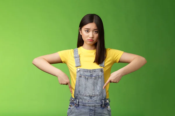 Triste ragazza asiatica in disperazione si sentono sconvolti, accigliato imbronciato pessimista, puntando verso il basso guardare la fotocamera tirando dolore faccia a disagio, esprimere tristezza e frustrazione, stand sfondo verde — Foto Stock