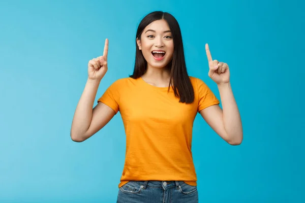 Amused chica asiática introducir nuevo producto compartir promo con usted, levantar las manos señalando los dedos hacia arriba sonriendo ampliamente, mirada emocionada y optimista, publicidad entusiasta, stand fondo azul — Foto de Stock