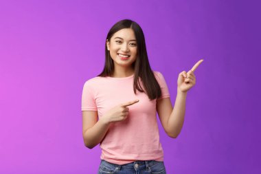 Neşeli, cana yakın, güler yüzlü Asyalı kız tanıtım yapıyor, yeni ürünleri tanıtıyor, neşeyle sırıtıyor havalı reklamlar sunuyor, pembe tişörtlü, pembe tişörtlü, arka planda eğleniyor.