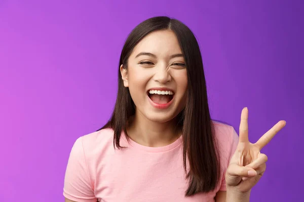 Headshot sincère insouciant rire asiatique fille s'amuser, montrer signe de victoire de la paix, regarder joyeusement caméra, exprimer enthousiasme et bonheur, profiter de drôle de compagnie amicale, stand fond violet — Photo