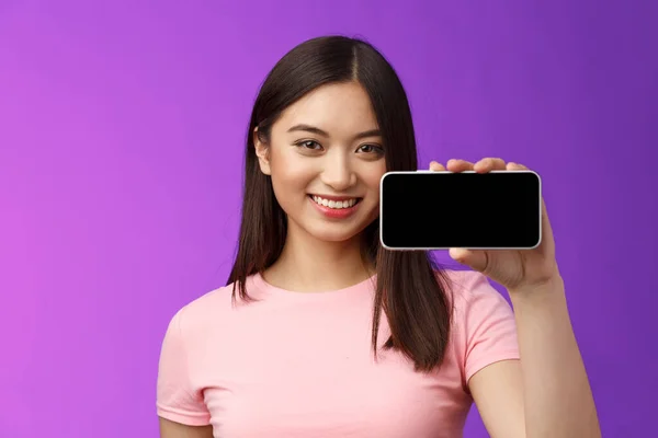 Närbild glad söt asiatisk kvinna hålla smartphone horisontellt, visa telefonskärmen, införa awesome nya program, spela intressant telefonspel, stå lila bakgrund främja — Stockfoto