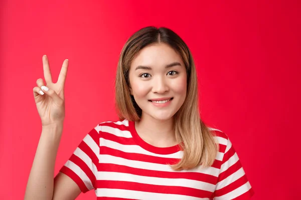 Close-up alegre alegre jovem mulher loira atraente usar listrado t-shirt sorrindo amigável fazer a ordem, reserva para dois show vitória sinal de paz, stand fundo vermelho, quer ser o segundo — Fotografia de Stock