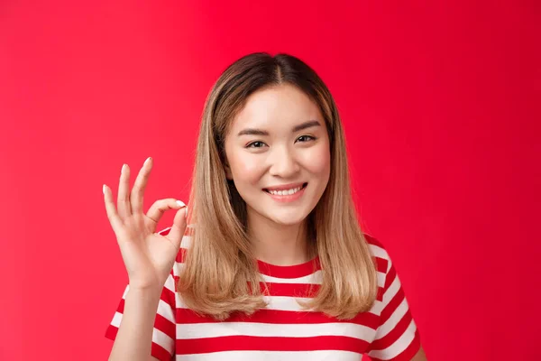 Close-up barátságos elégedett gondtalan fiatal ázsiai szőke lány show jóváhagyás ítélőképesség jel oké, egyetért terv jó mosolygós nagyjából, mint az ötlet elégedett nagy választás, állni piros háttér boldog — Stock Fotó
