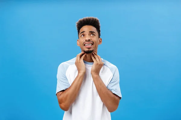 Mann, der an Allergie leidet, juckt in der Kehle Grimassen vor Unbehagen und Unbehagen hält Finger am Hals und blickt mit enttäuschtem Gesichtsausdruck auf, der sich vor blauem Hintergrund krank fühlt — Stockfoto