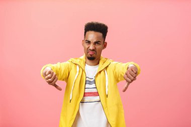 Kesinlikle nefret ediyorum. Korkunç bir şey. İğrenç ve hoşnutsuz Afro-Amerikan erkek, sakallı ve afro saçlı, kaşlarını çatmış dudaklarını buruşturmuş, pembe duvarın üstünde baş parmaklarını eğerek jest yapıyor.