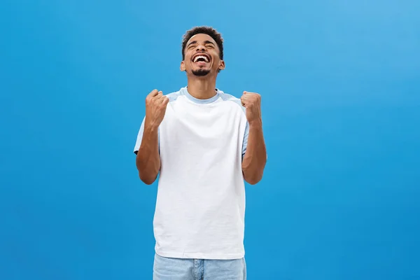 Africano americano homem sendo feliz finalmente ganhando sucesso alcançando a vitória levantando dentes apertando regozijando-se da felicidade sorrindo alegremente levantando a cabeça para cima celebrando triunfo sobre fundo azul — Fotografia de Stock