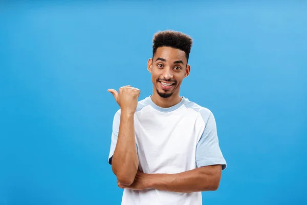 Attractive skillful coworker indicating at friend who can solve situation standing relaxed and carefree over blue background pointing left or backwards with thumb and smiling while casually talking — Stock Photo, Image