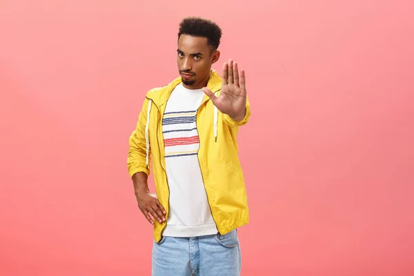 Тримайтеся не рухатися. Портрет інтенсивного красивого темношкірого хлопця в модному вбранні, що тягне долоню в попереджувальний жест, вимагаючи зупинити або підкоритися правилам на рожевому тлі — стокове фото