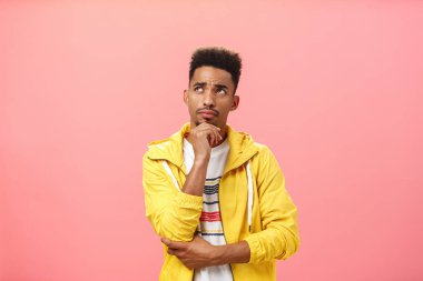 Düşünceli, koyu tenli, sakallı, afro saçlı, kaşlarını çatmış, çenesi çatık, sol üst köşeye odaklanmış pembe arka plan üzerinde karar veren düşünceli, sorunlu genç adamın stüdyo fotoğrafı.