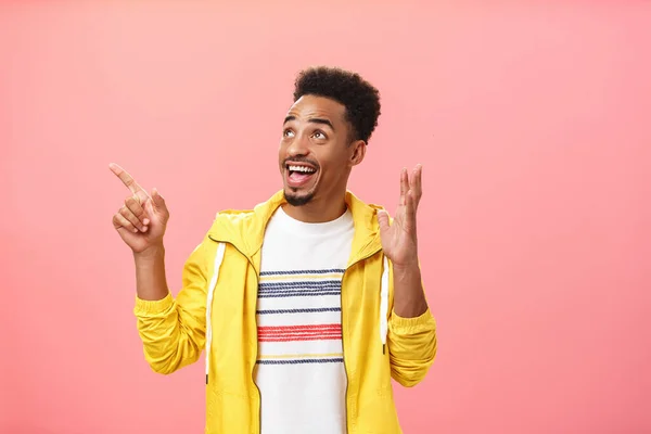 Opgewonden en opgewonden donkere huid jonge man met baard en afro kapsel hef palm in verbazing houding wijzen en kijken naar de linker bovenhoek verbaasd en verrukt over roze muur — Stockfoto