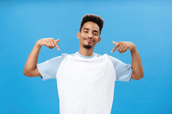 Sim, olha como sou fixe. Orgulhoso arrogante e elegante homem de pele escura com barba a guinchar e a sorrir com prazer apontando para si mesmo a falar de realizações pessoais sobre fundo azul — Fotografia de Stock