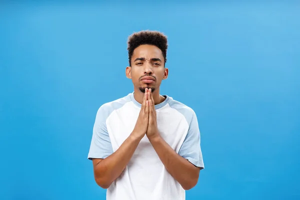 Waist-up shot of concerned intense handsome african american boyfriend with beard holding hands in pray frowning looking thoughtful at camera making important calculations over blue wall — Stock Photo, Image
