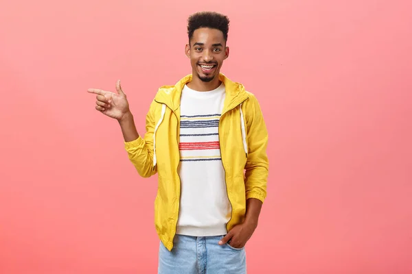 Friendly helpful male dark-skinned friend showing girlfriend appartment pointing left at living room smiling joyfully hanging out in funny and amusing company over pink background — Stock Photo, Image