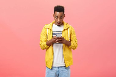 Erkek arkadaşı, elinde akıllı telefonuyla ekrandan etkilenmiş bir şekilde pembe arka planda harika bir uygulama çalarken dudakları kıvrılmış bir şekilde hayret verici bir şekilde hayret verici bir mesaj almış.