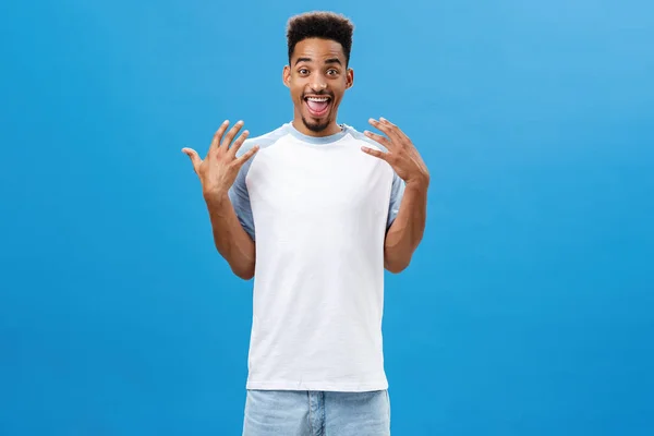 Entusiástico satisfeito afro-americano irmão em t-shirt com barba tremendo palmas com emoção e alegria sorrindo alegremente explicando truque incrível que ele faz enquanto patina sobre fundo azul — Fotografia de Stock