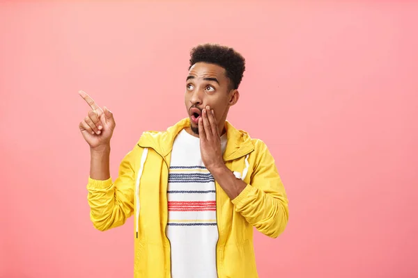 Speechless intrigued and excited african-american male with beard and afro hairstyle saying wow and gasping holding palm near opened mouth looking and pointing at upper left corner amazed — Stock Photo, Image