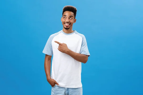 Homem americano africano criativo com barba e corte de cabelo afro apontando e olhando para o canto superior esquerdo sendo encantado e satisfeito com o clima perfeito e grande empresa sobre fundo azul — Fotografia de Stock