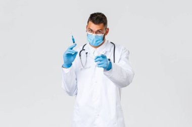 Covid-19, sağlık çalışanları, salgın hastalıklar ve virüs önleme konsepti. Beyaz önlüklü, tıbbi maskeli ve eldivenli kararlı doktor. Elinde Coronavirus aşısı olan şırınga var.