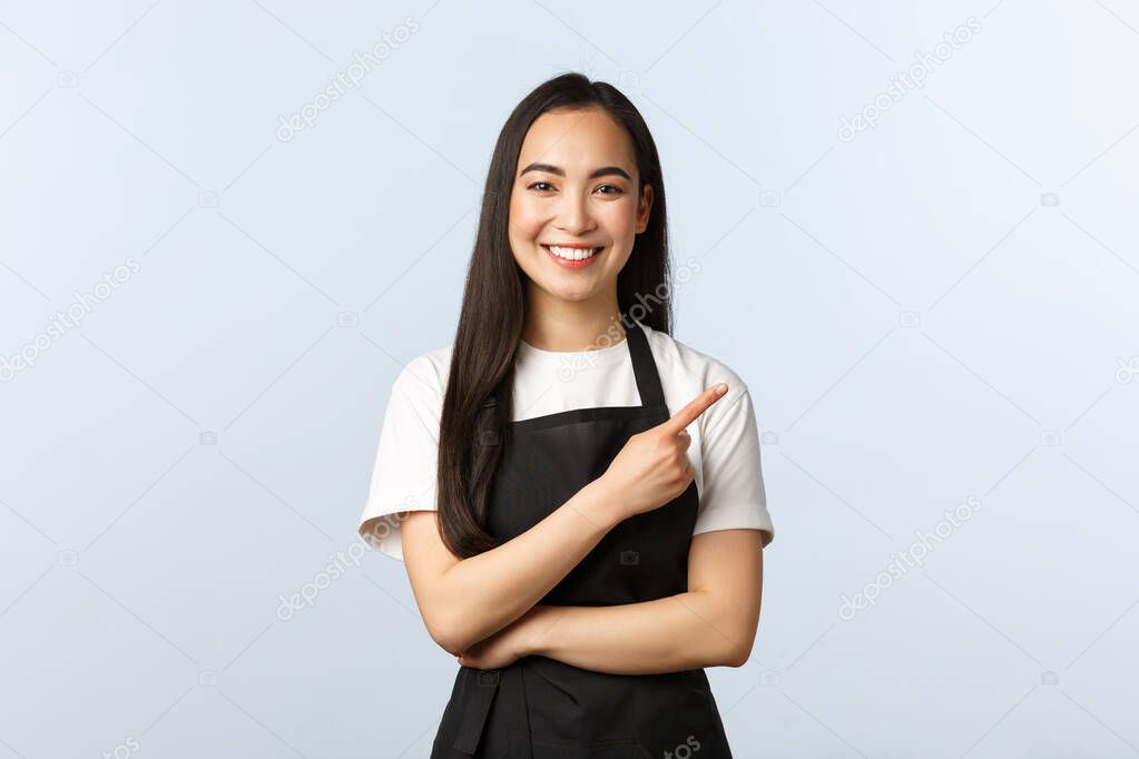 Coffee shop, small business and startup concept. Cheerful asian girl in apron working restaurant or cafe, inviting consumers for special offer. Smiling female staff pointing finger right