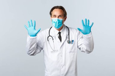 Covid-19, virüsü önleme, sağlık çalışanları ve aşı konsepti. Beyaz önlüklü, tıbbi maskeli ve eldivenli heyecanlı erkek doktor.