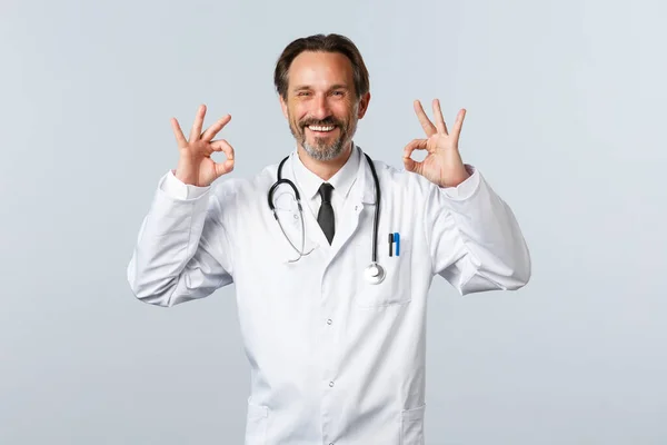 Covid-19, ξέσπασμα του ιού της στέψης, επαγγελματίες υγείας και πανδημία. Ικανοποιημένος χαρούμενος γιατρός εγγυάται την ποιότητα. Ψυχολόγος δείχνουν εντάξει χειρονομία και χαμογελώντας ευχαριστημένος, διαφημίζουν promo — Φωτογραφία Αρχείου